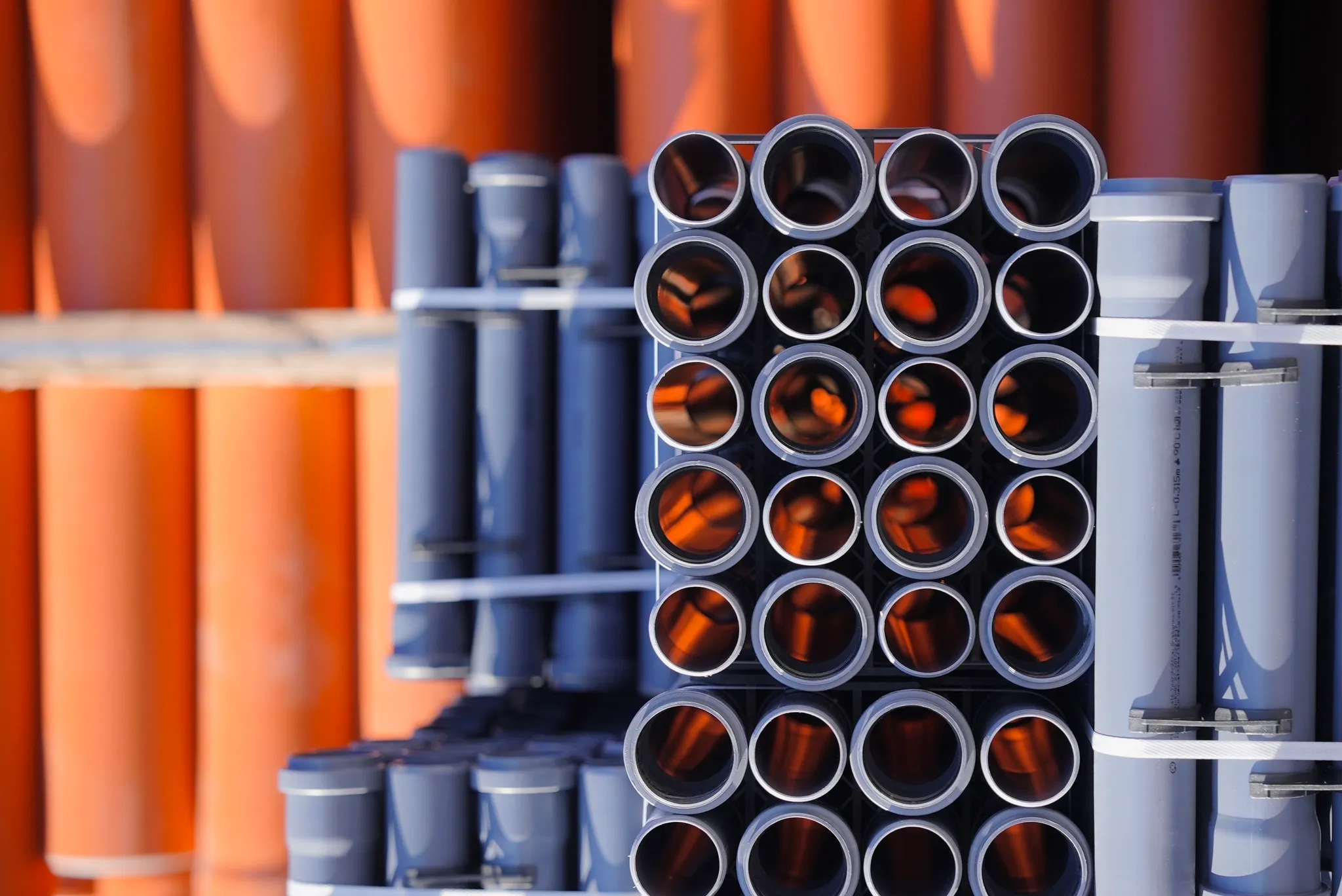 Równo ułożone szare rury kanalizacji wewnętrznej Drewplast na tle rur kanalizacji zewnętrznej.