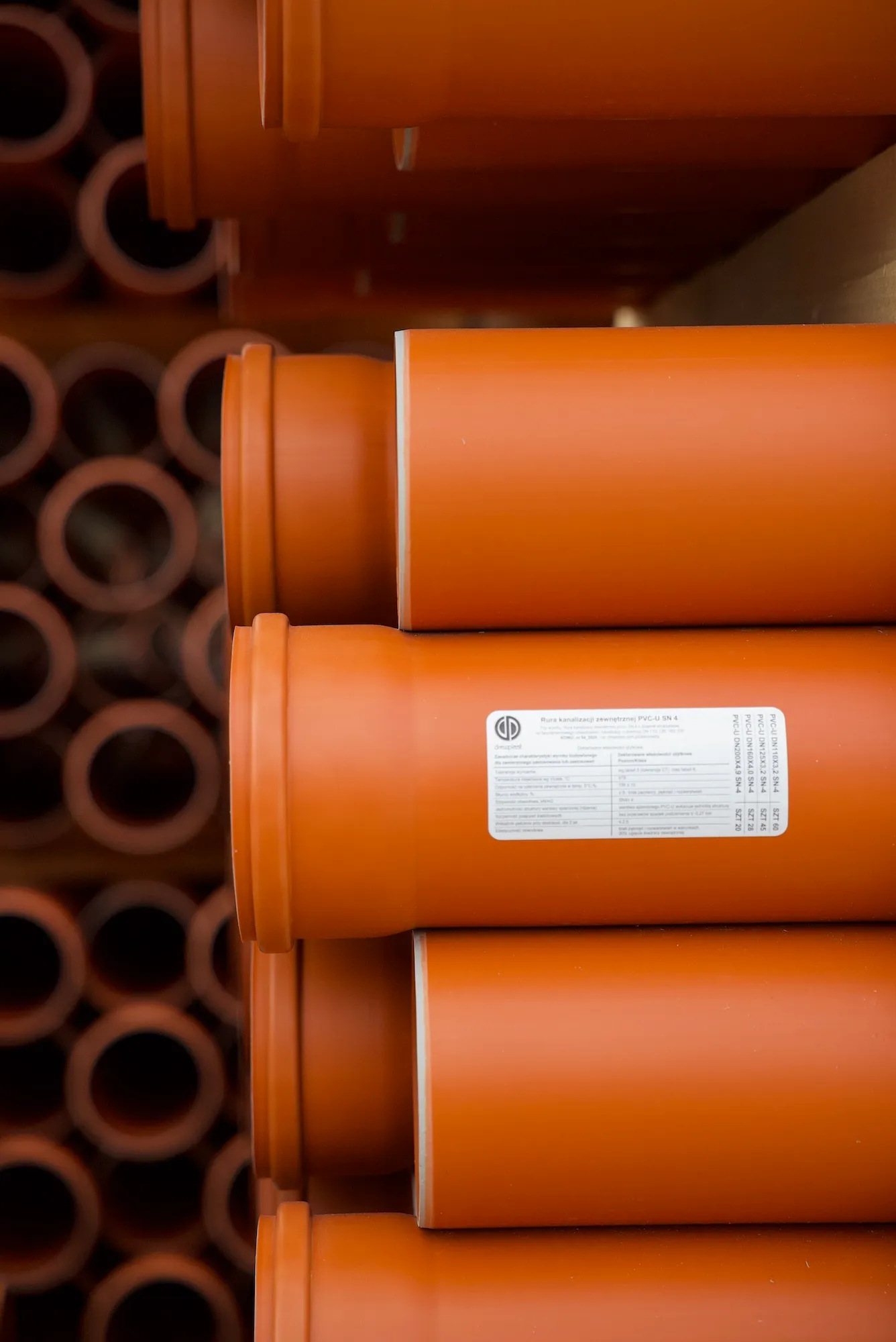 Rury kanalizacji zewnętrznej o ceglanym kolorze, ułożone poziomo w schludnym układzie.