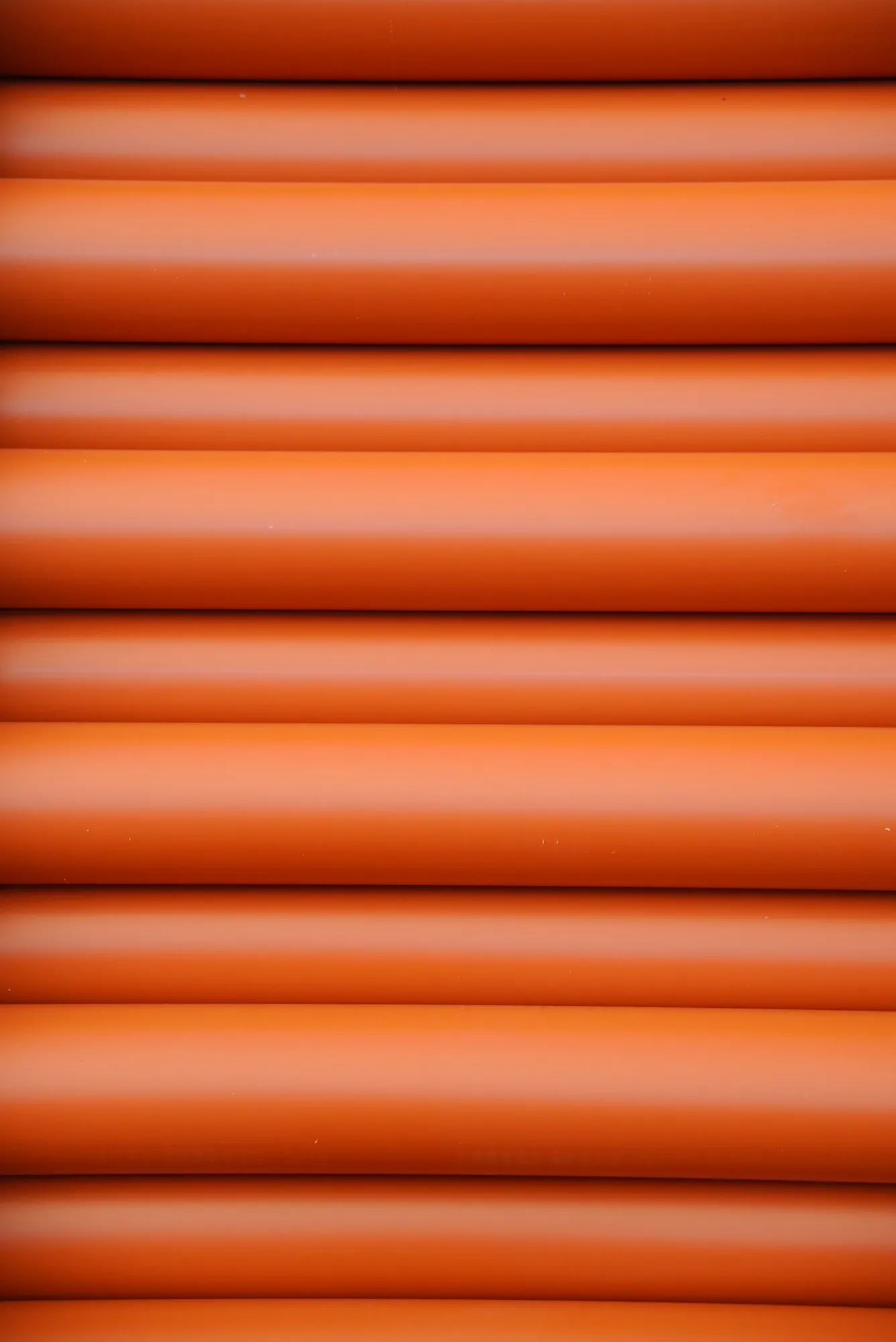 Rury kanalizacji zewnętrznej o ceglanym kolorze, ułożone poziomo w schludnym układzie.