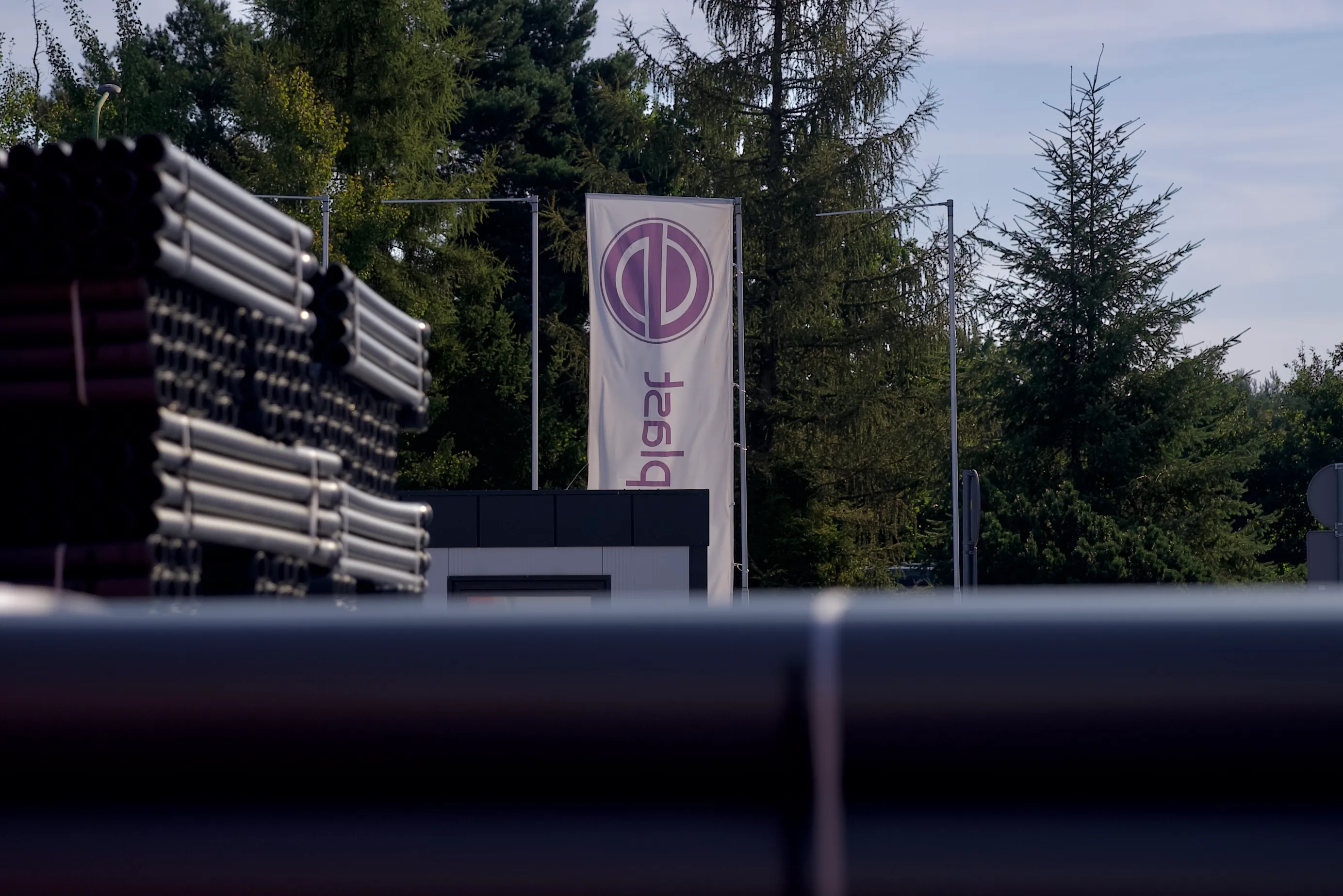 Plac zakładu produkcyjnego Drewplast z flagą firmową i magazynem rur kanalizacyjnych.