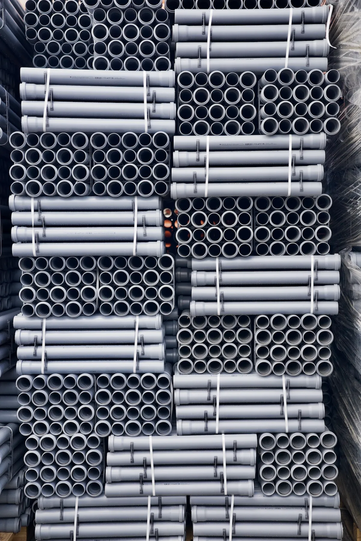 Szare rury kanalizacji wewnętrznej, starannie ułożone w miejscu składowania.