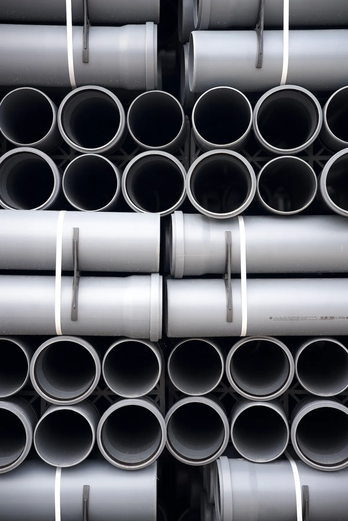 Szare rury kanalizacji wewnętrznej, starannie ułożone w miejscu składowania.